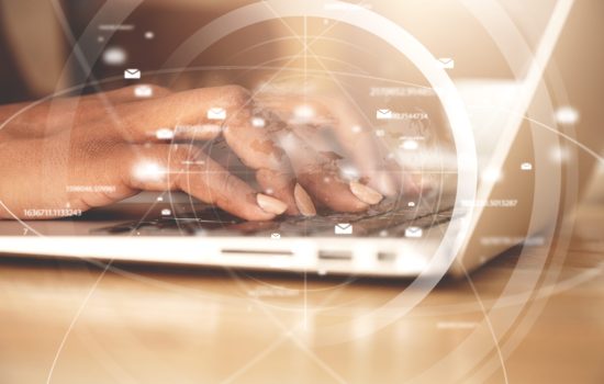 Worldwide connection interface. Double exposure of African American businesswoman typing a message via e-mail using laptop while sitting at the wooden table in the office. Selective focus on hands