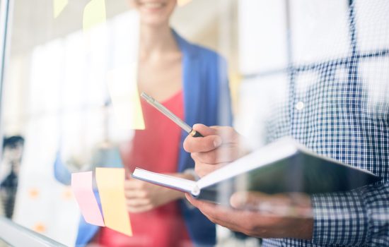 Manager with open notebook and pen pointing at one of reminders on noteboard