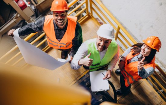 Three factory workers in safety hats discussing manufacture plan